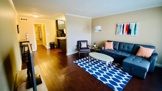 A living room with a dark-colored sectional sofa, a small white coffee table, and a blue patterned rug. - Near Downtown Stunning Course-View Flat (Birmingham)