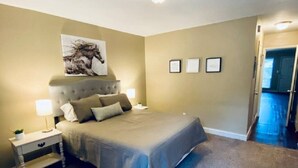 A bedroom with a bed, nightstands, a wall-mounted artwork, and a door leading to another room. - Near Downtown Stunning Course-View Flat (Birmingham)