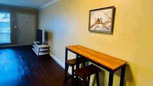 A room with a wooden floor, a desk with two chairs, a framed picture on the wall, and a door with a window. - Near Downtown Stunning Course-View Flat (Birmingham)