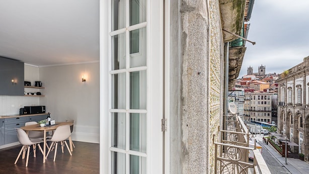 A modern kitchen with a dining area, a large window, and a view of historic buildings. - GuestReady - Bourse Maison (Porto)