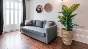 A grey sofa with cushions, a large woven plant pot, and two wall decor pieces. - GuestReady - Bourse Maison (Porto)