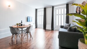 A modern living room with a wooden dining table, grey chairs, a grey sofa, and a large green plant. - GuestReady - Bourse Maison (Porto)