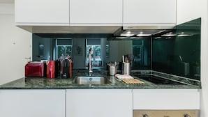 Una cocina moderna con un lavamanos de acero inoxidable, un horno empotrado y un microondas. Hay dos electrodomésticos rojos en la encimera, y un bloque para cuchillos con utensilios.