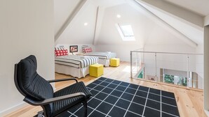 Un dormitorio en ático con techos altos, un tragaluz, dos camas con ropa de cama a rayas, una silla negra y un otoman amarillo.