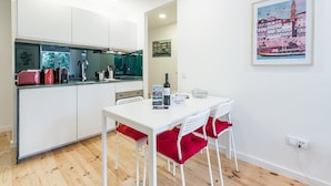 Una cocina moderna con armarios blancos, una mesa de comedor con cojines rojos y un cuadro con un paisaje urbano en la pared.