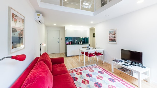 Un apartamento moderno con sala de estar que incluye un sofá rojo, televisor y comedor con una pequeña mesa y sillas.