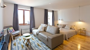 A modern, well-lit room with a sofa, a bed, a small table, and a chair.