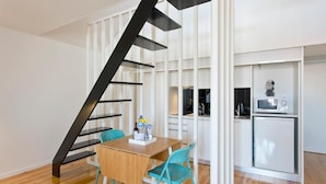 A modern kitchen with a built-in microwave and refrigerator, a wooden dining table with two chairs, and a black staircase leading to an upper level.