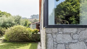 A stone building with a large window reflecting trees and a garden. - GuestReady - Chapel`s Garden (Caminha)