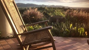 A wooden chair with a woven backrest on a tiled patio overlooking a garden with various plants and a distant mountain range. - Your home away from home on the Farm, 4 Casitas Bed n Breakfast - Casita 2 (Cabo Rojo)