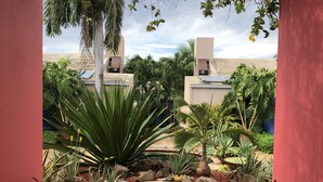 A modern outdoor area with a concrete pathway, various tropical plants, and a water feature. - Your home away from home on the Farm, 4 Casitas Bed n Breakfast - Casita 2 (Cabo Rojo)