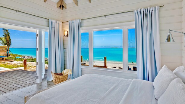 A bedroom with a large bed, a view of the beach, and a wooden deck.