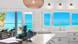 A modern kitchen with large windows, a central island, and hanging pendant lights.