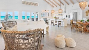 A spacious living area with a high ceiling, wicker furniture, and a view of the ocean.