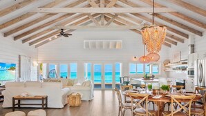 A spacious living area with a large sofa, dining table, and chairs, a ceiling fan, and a view of the ocean.