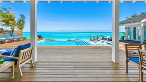A wooden deck with lounge chairs and a pool overlooking a clear blue sea.