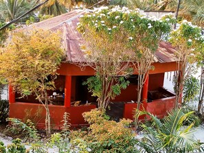 A small, red-roofed structure surrounded by various plants and trees. - Family Holiday House (Jambiani)