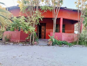 Un edificio con fachada roja, puerta de madera y un pequeño jardín con plantas en macetas.