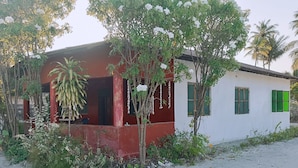 Un edificio con fachada roja, un pequeño porche y una pared blanca con contraventanas verdes.
