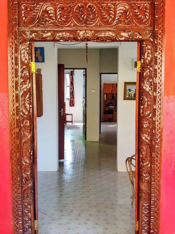 Un pasillo con puertas de madera decoradas que conducen a una habitación con piso de baldosas y pared roja.