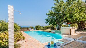 A swimming pool with a tiled deck, a lounge chair, and a table with drinks. - Authentic Sicilian Charm With Pool, Sea View, Parking & Wifi (Avola)