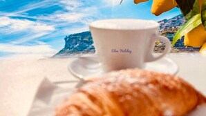 A croissant and a cup of coffee on a table with a scenic view in the background. - Eden Holiday Apartment (Minori)