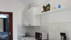A compact kitchen with a washing machine, a microwave, and a coffee maker. - Eden Holiday Apartment (Minori)