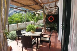 A covered outdoor patio with a table and chairs, a potted plant, and a lifebuoy on the wall. - Eden Holiday Apartment (Minori)