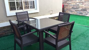 A patio with a glass-top table and wicker chairs, a stone wall, and a window with white frames. - Room-adanma Hotel and Suites - Guest Roo (Abuja)
