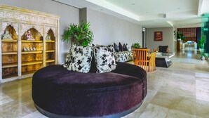 Eine moderne Lobby mit einer runden schwarzen Sitzecke, einem Holzschrank mit Dekorationselementen und einem Empfangsbereich.