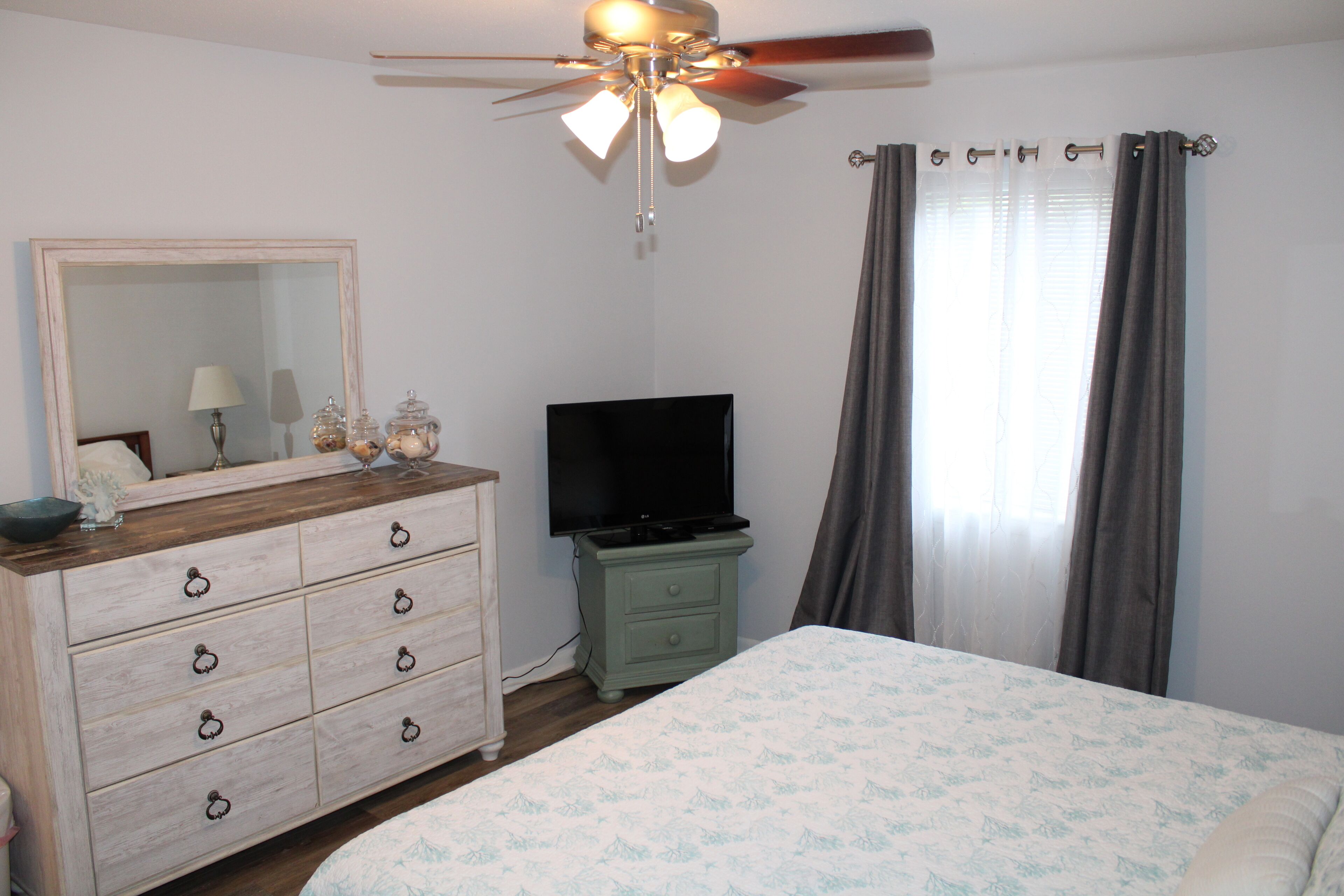 Une chambre à coucher comprenant un lit, une commode, un téléviseur et un ventilateur de plafond.