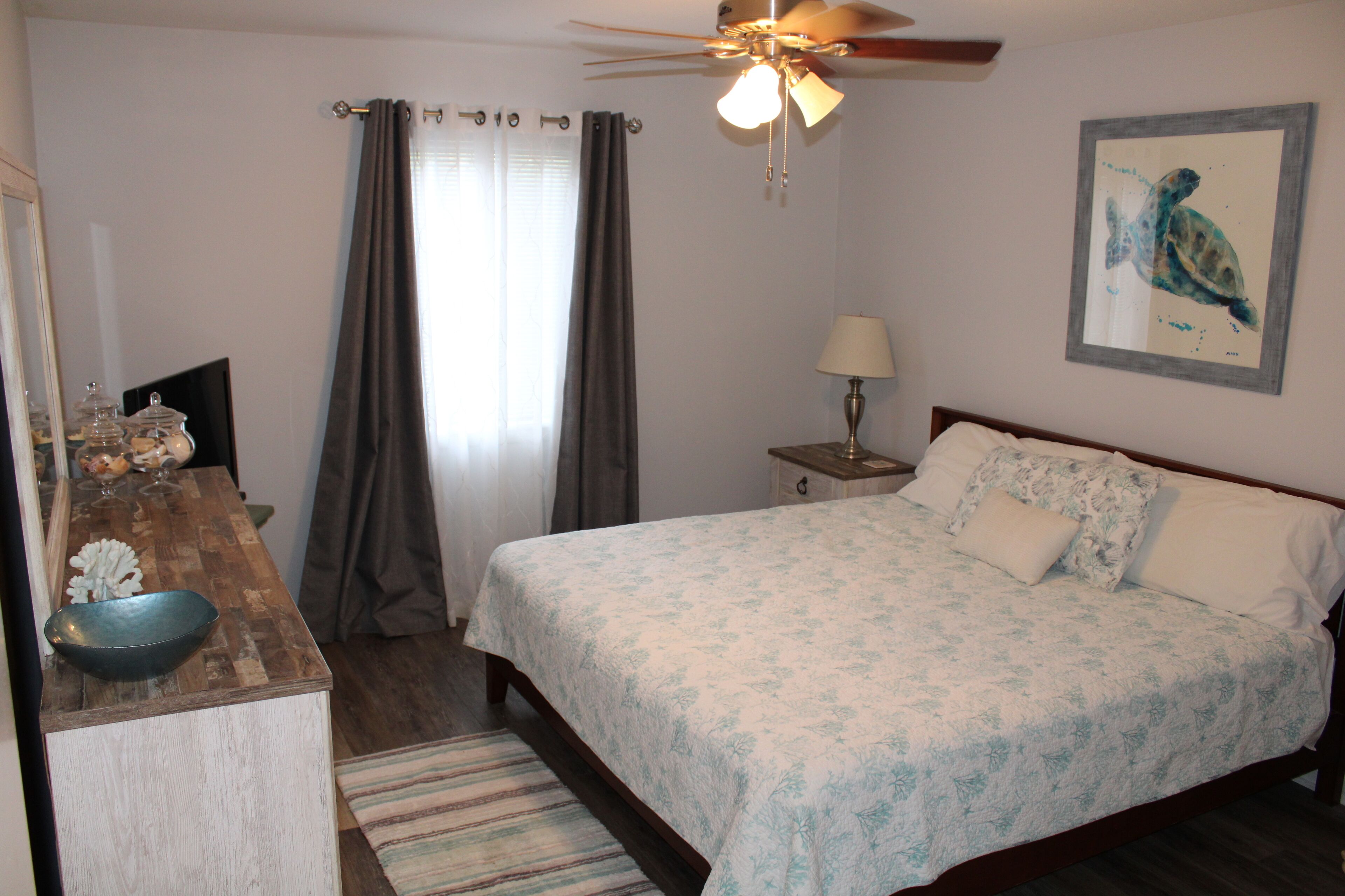 A bedroom with a bed, a desk, a lamp, and a ceiling fan.