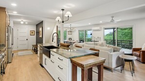 A modern kitchen with a large island, white cabinetry, and a wooden dining table. - Hideaway at Harvest Moon (Sylva)