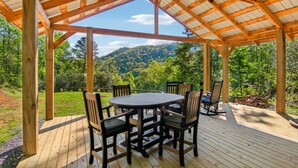 A wooden deck with a covered patio, a round table, and six chairs. - Hideaway at Harvest Moon (Sylva)