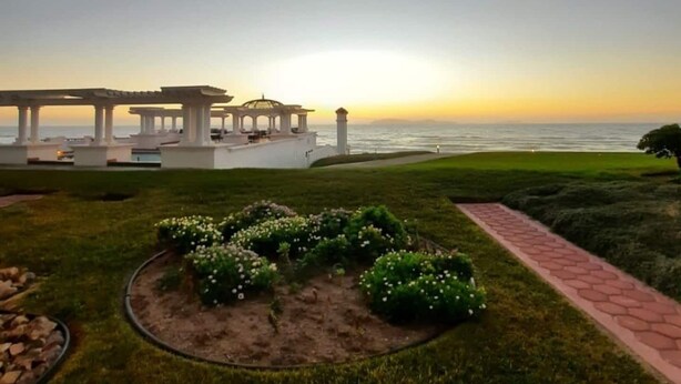 A garden with a paved path, a gazebo, and a view of the ocean at sunset. - Ocean view beautiful apartament with pool and jacuzzi, furnished. (Tijuana y Rosarito)