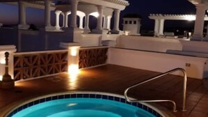 A swimming pool with a tiled edge, surrounded by a wooden deck and white columns. - Ocean view beautiful apartament with pool and jacuzzi, furnished. (Tijuana y Rosarito)