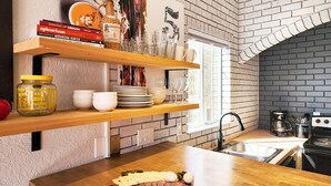 Una cocina con estantes de madera, pared de ladrillo y encimera de madera con una tabla de embutidos.