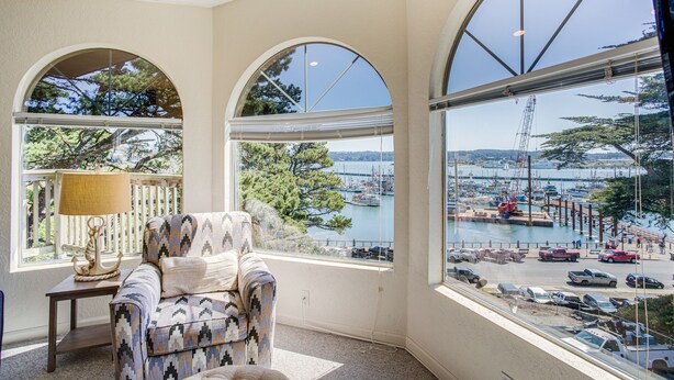 Quarto com uma grande janela com vista para uma marina, uma poltrona estampada e um abajur sobre uma mesinha lateral.