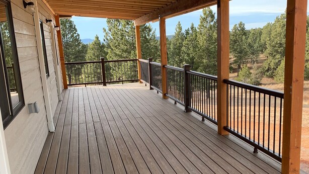 A wooden deck with a railing, overlooking a forested area. - Western Blue Skies in Country (Hot Springs)