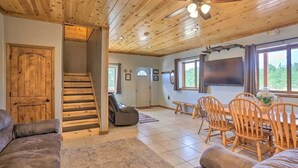 A spacious living area with a wooden staircase, a ceiling fan, a large flat-screen TV, and a dining table with chairs. - Western Blue Skies in Country (Hot Springs)