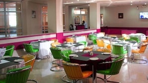 A dining area with round tables, green and orange chairs, and a pink accent wall. - Room-agura Hotel - Guest Room (Abuja)