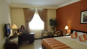 A hotel room with a bed, a desk with a computer, a chair, a lamp, and a television. - Room-agura Hotel - Guest Room (Abuja)