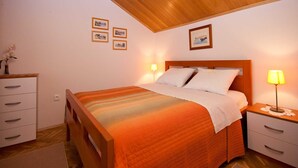 Quarto com teto de madeira, cama com colcha laranja, duas mesas de cabeceira com luminárias, um criado-mudo e uma cômoda com gavetas.