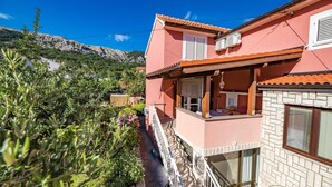 Um edifício rosa com varanda, aparelhos de ar condicionado e vista para uma paisagem montanhosa.