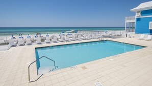 Ein Poolbereich mit Blick auf den Ozean, ein Gebäude mit blauer Fassade und eine geflieste Terrasse mit Liegestühlen.