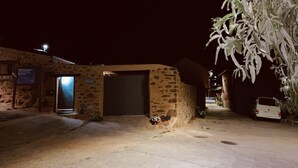 A stone building with a closed door, a small garden area with potted plants, and a parked car. - THE WONDER Legalized VUT-LE-533 (Tedejo Folgoso de la Ribera. león)