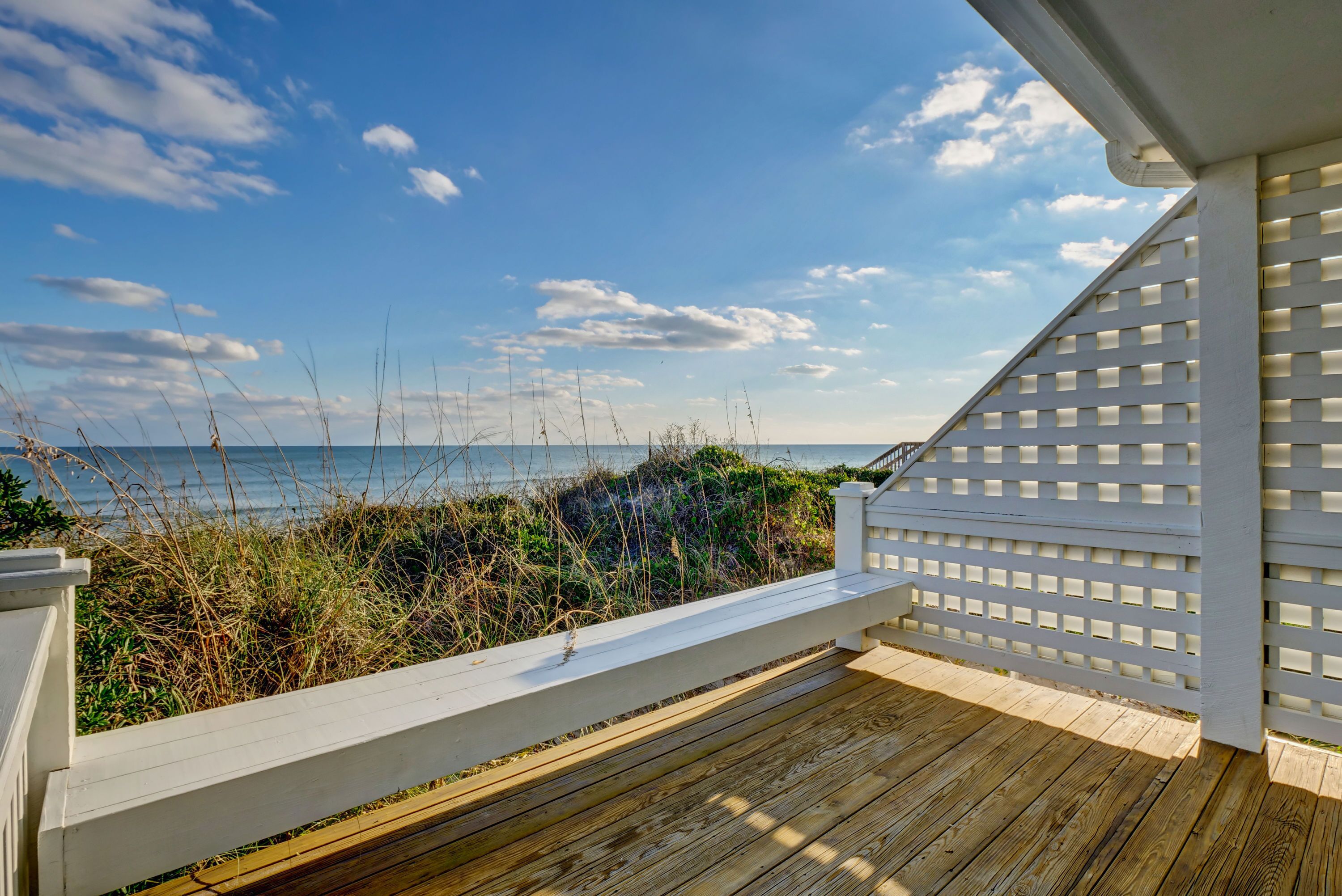 A wooden deck with a white lattice railing overlooking a beach.
