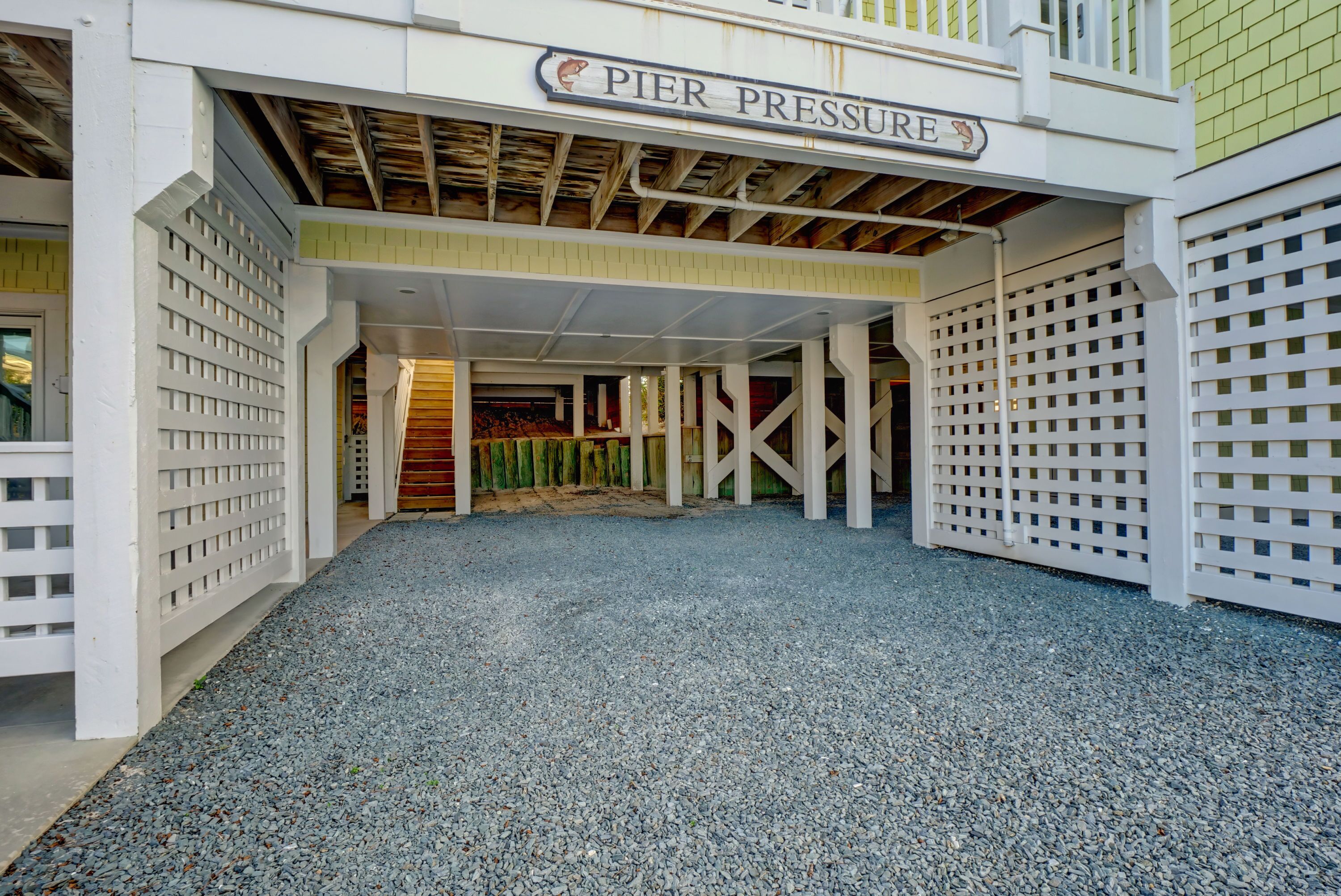 A covered entrance to Pier Pressure with a gravel driveway and white lattice railings.