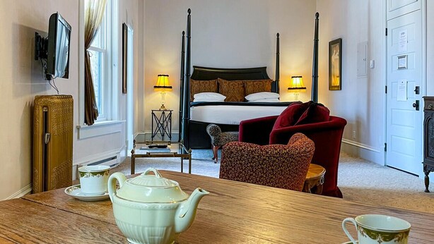 Een kamer met een houten tafel gedekt voor thee, een bed met hemelbed, een rode stoel en een vintage radio.