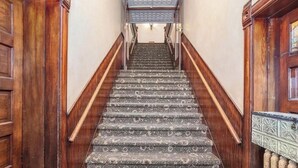 Een trap met een kamerbreed tapijt, houten leuningen en een metalen balustrade.